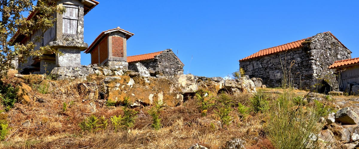 A stone building with a red-tiled roof, surrounded by dry grass and rocks.