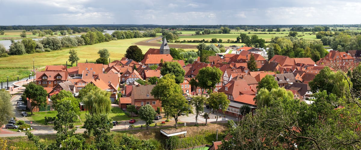 A village with red-roofed houses, a church, and a river in the background.