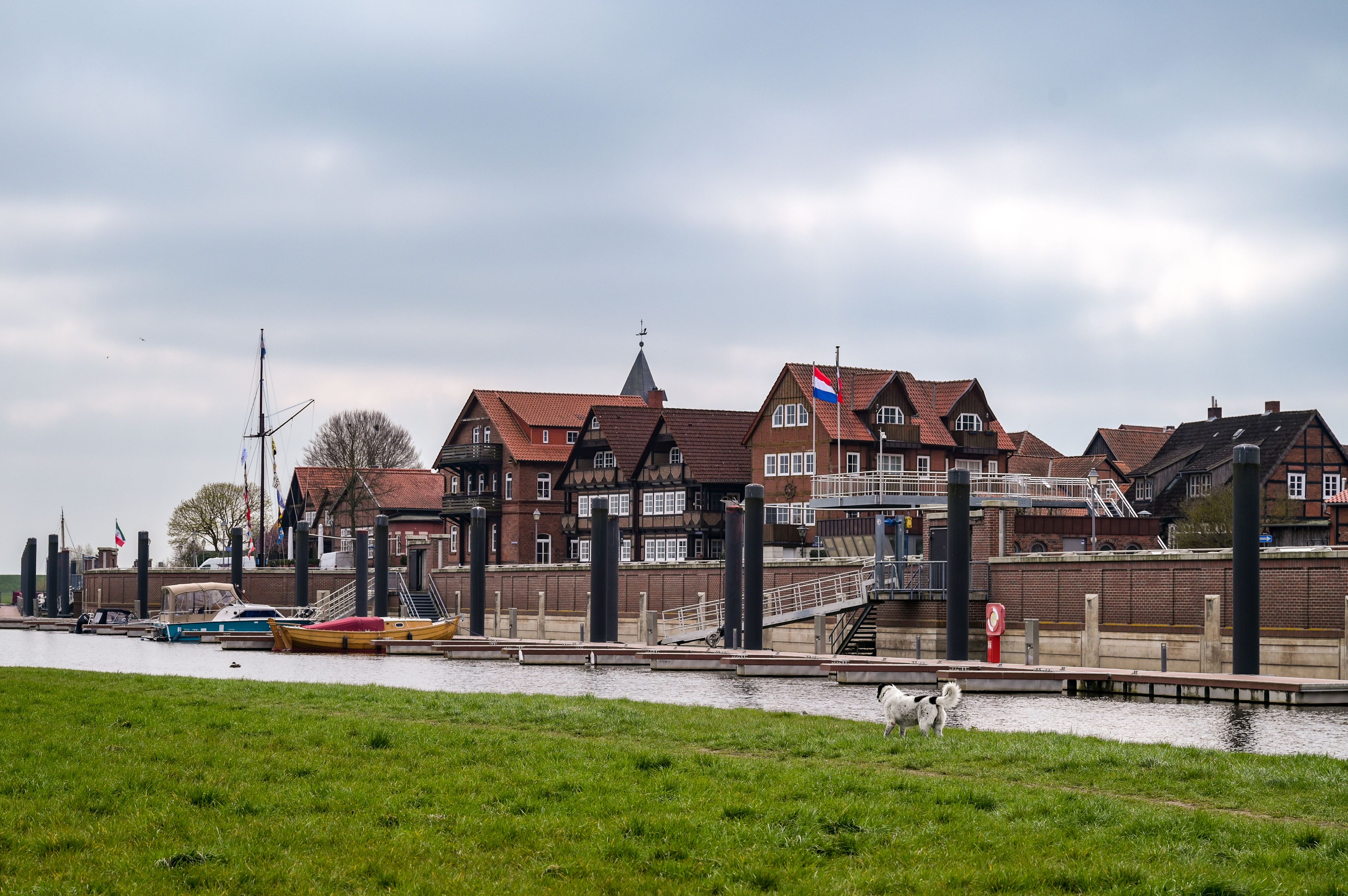 A riverside town with traditional houses, a dock with boats, and a grassy area.
