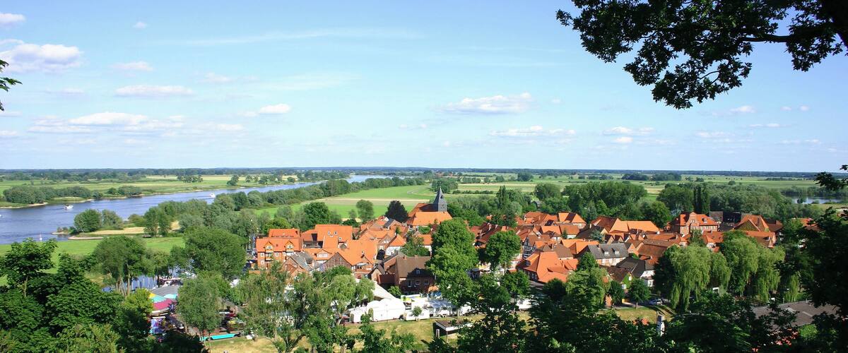 A riverside town with red-roofed houses, a church steeple, and lush greenery.