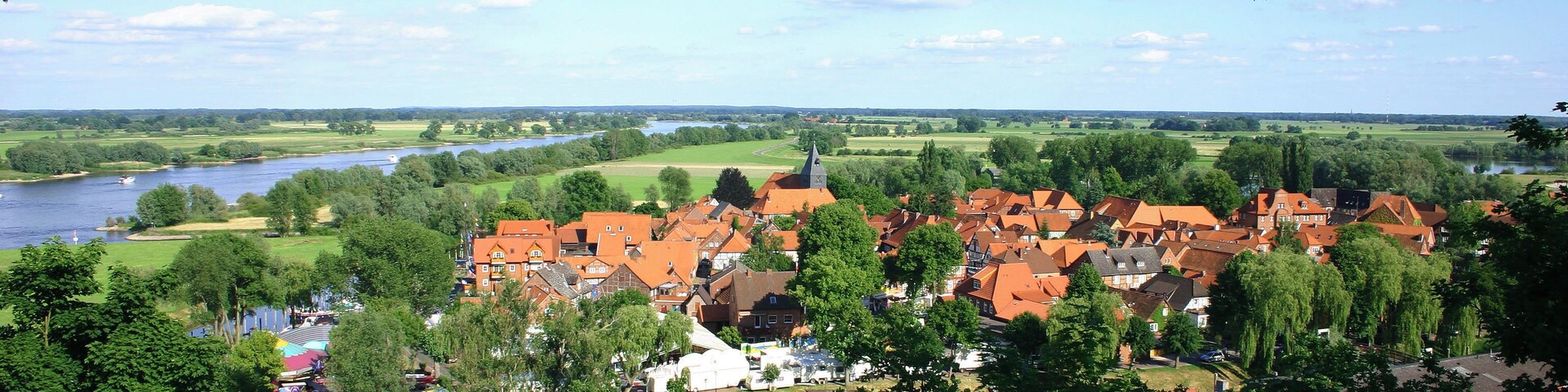 A riverside town with red-roofed houses, a church steeple, and lush greenery.