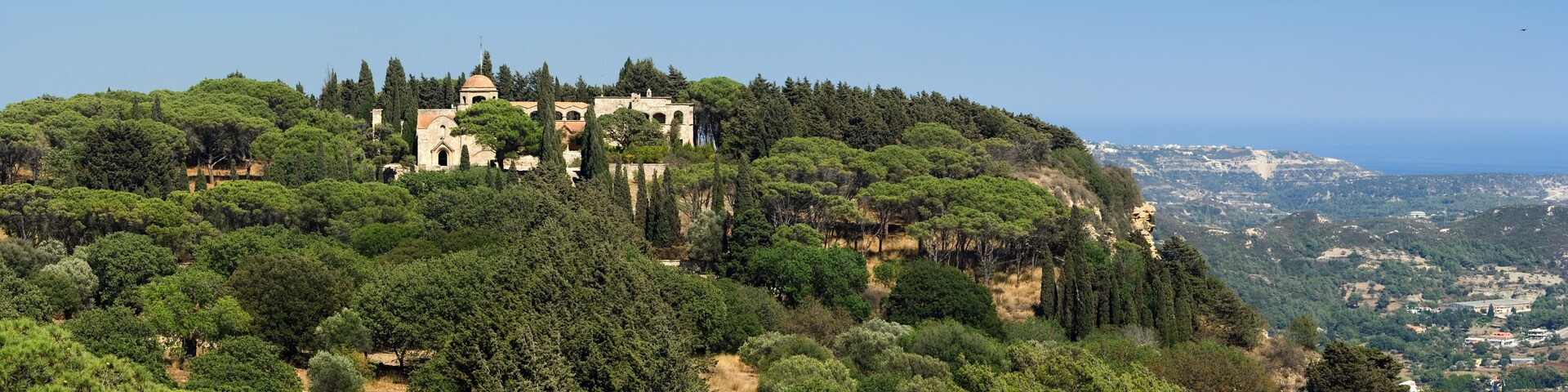 Un château historique perché sur une colline, entouré d’une forêt dense et dominant un paysage côtier.