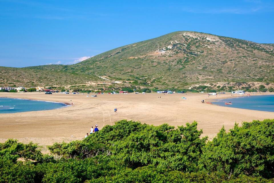 A beach with a mountain in the background, clear skies, and sparse vegetation.