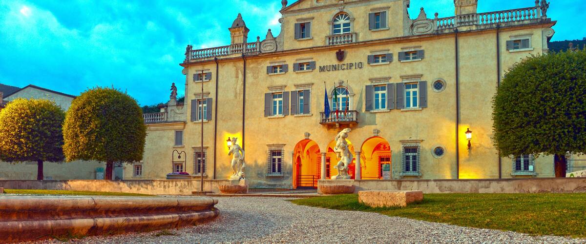 A historic building with a central archway, statues, and a well-maintained garden.