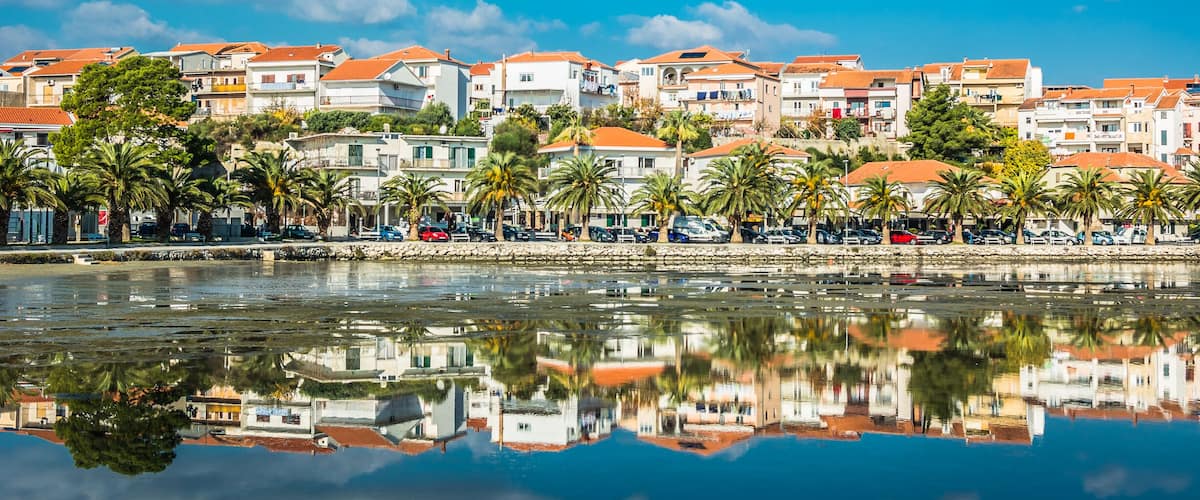 A coastal town with buildings, palm trees, and a calm sea.