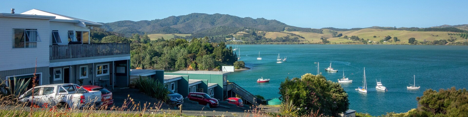 Un pueblo costero con un puerto deportivo, coches aparcados y barcos en el agua.