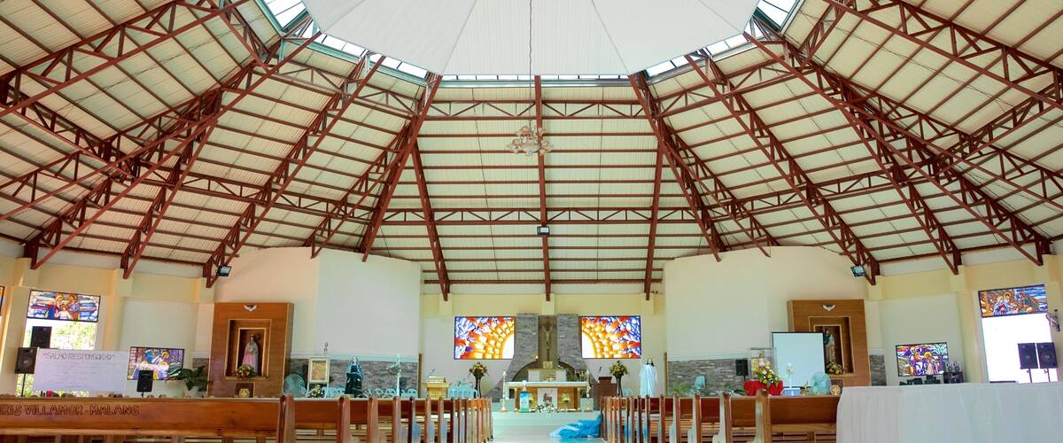 A church interior with a high arched ceiling, wooden pews, stained glass windows, and a central altar.