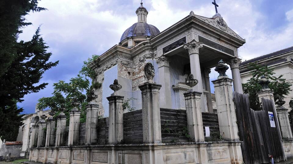 A historic building with a dome and columns, surrounded by trees and a fence.