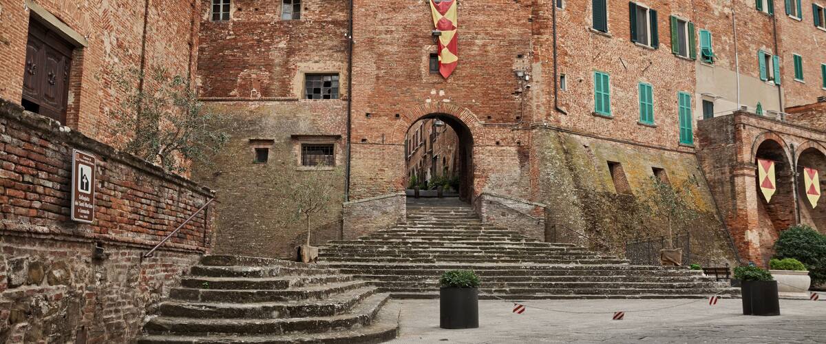 A historic building with a red and white striped flag, brick walls, and a staircase leading to an entrance.