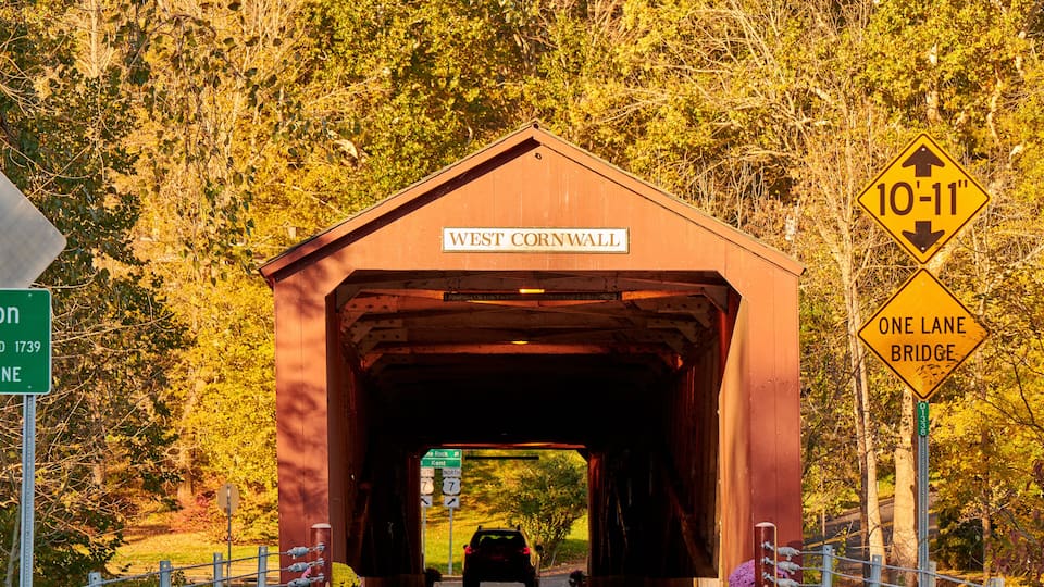 A covered bridge labeled "West Cornwall" with a sign indicating a height restriction of 10-11 inches and a one-lane bridge warning.