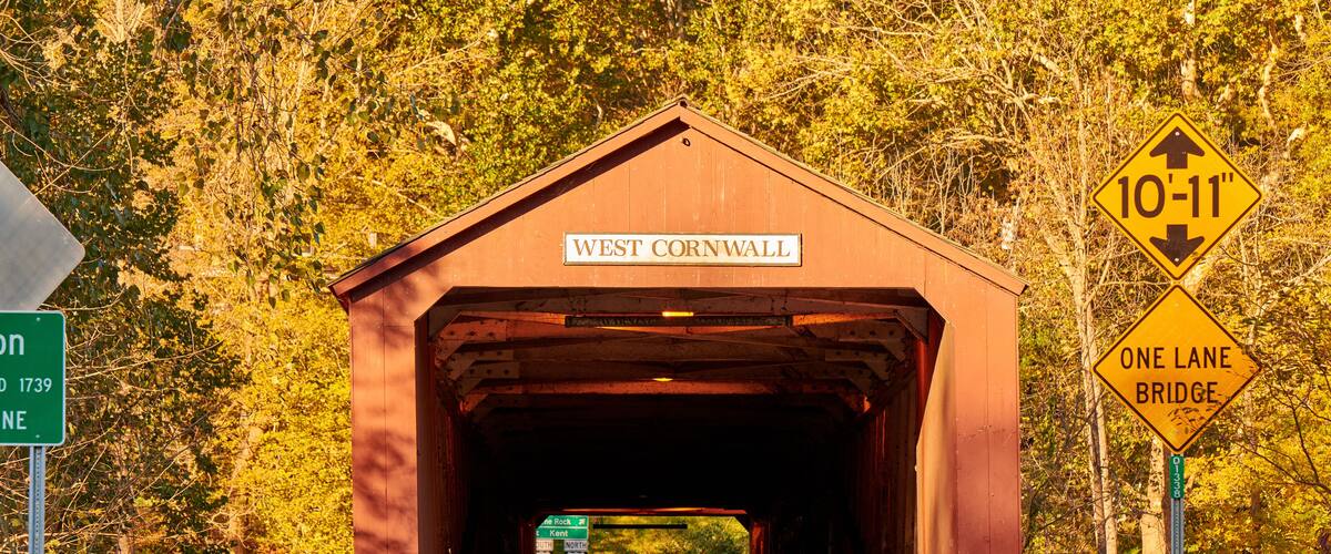 A covered bridge labeled "West Cornwall" with a sign indicating a height restriction of 10-11 inches and a one-lane bridge warning.