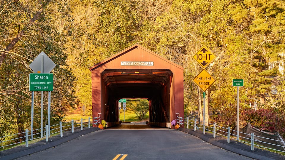 A covered bridge with signs for Sharon, West Cornwall, and a 10-11" bridge clearance.
