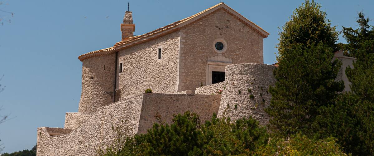 A stone church with a cross on top, surrounded by trees.