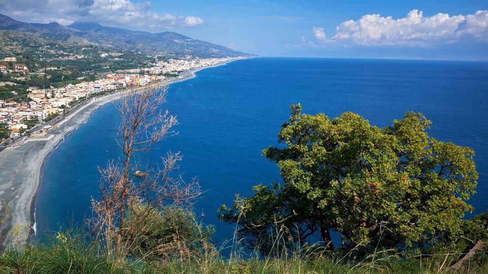 A coastal town with a beach, mountains, and a clear blue sea.