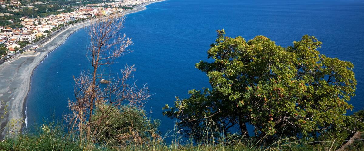 A coastal town with a beach, mountains, and a clear blue sea.