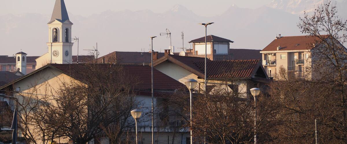 A town with a church tower, residential buildings, street lamps, and mountains in the background.