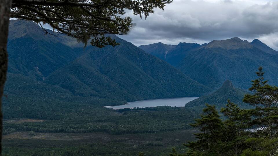 A mountainous landscape with a lake surrounded by dense forests and rugged peaks.