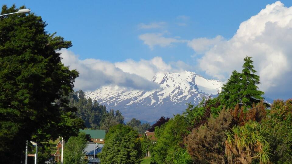 A snow-capped mountain, a clear sky, and a town with houses and trees.