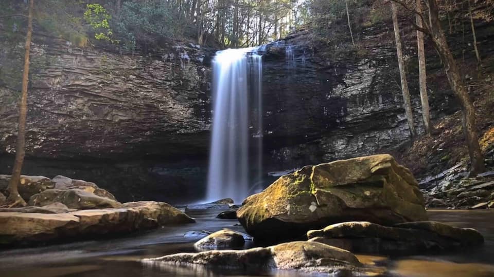 A waterfall in a forested area with large rocks in the foreground.
