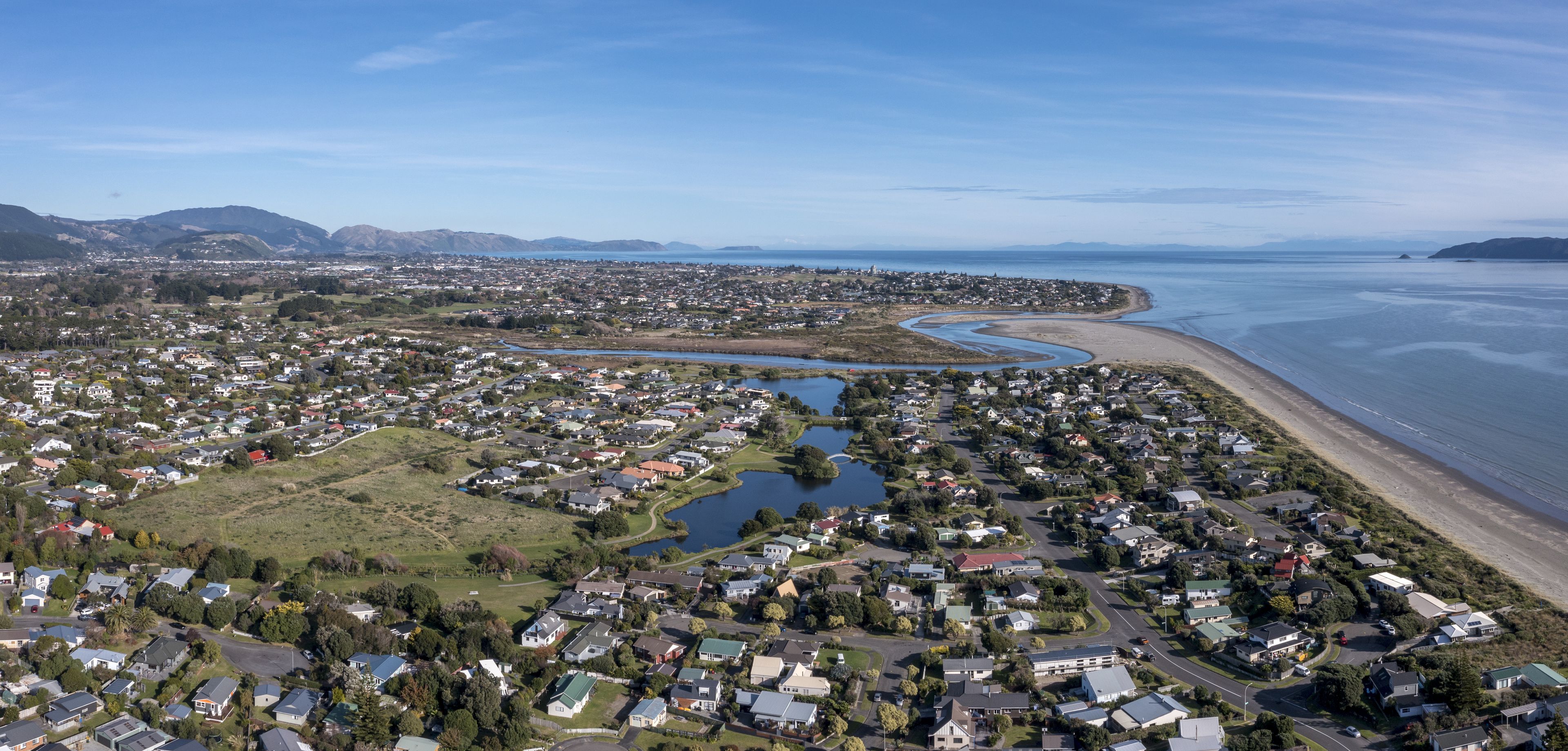 An aerial view of a coastal town with a river, residential areas, and a beach.