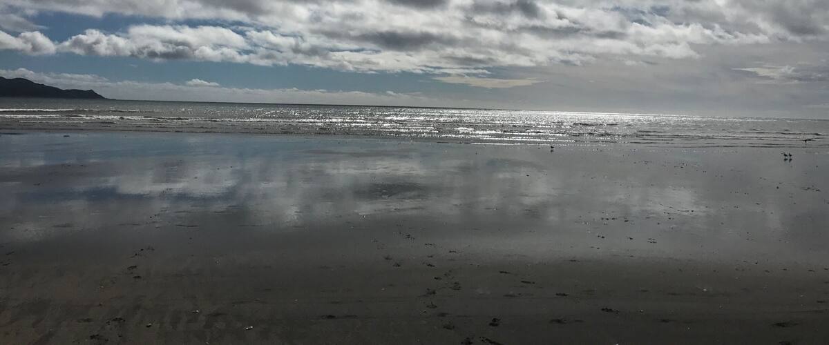 A beach with a cloudy sky and calm water reflecting the sky.
