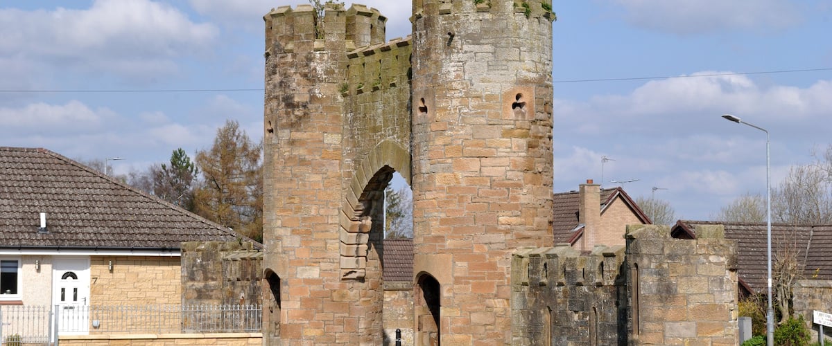 A medieval stone tower with arched openings and battlements, surrounded by residential buildings.