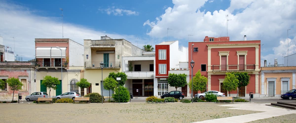 A street with colorful buildings, parked cars, and trees.