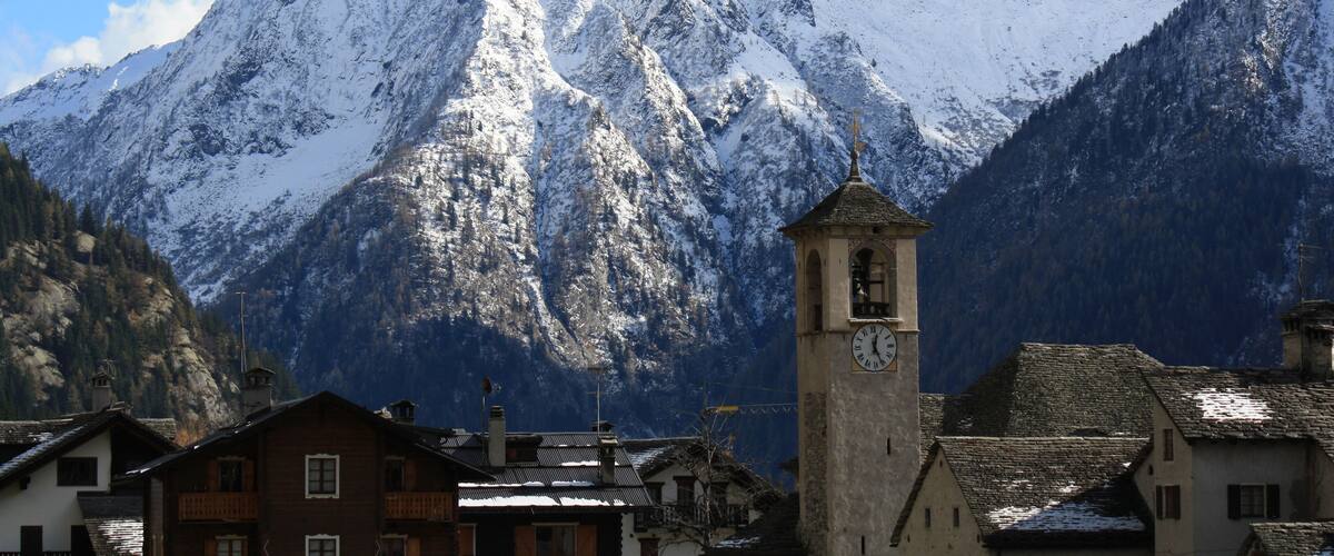 A snow-covered mountain range with a clock tower in a village.