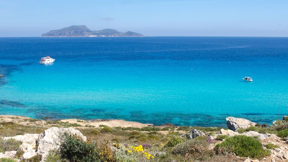 A coastal landscape with clear turquoise waters, rocky cliffs, and a distant island.