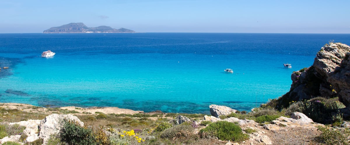 A coastal landscape with clear turquoise waters, rocky cliffs, and a distant island.
