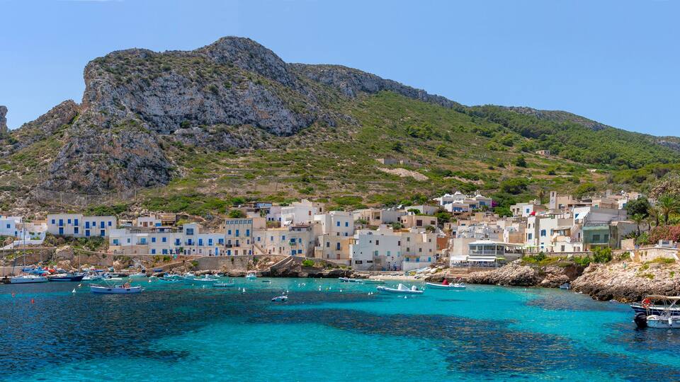 A coastal town with white buildings, a rocky mountain, and boats in the water.
