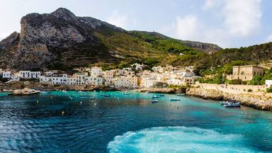 A coastal town with white buildings, a rocky mountain, and turquoise waters.