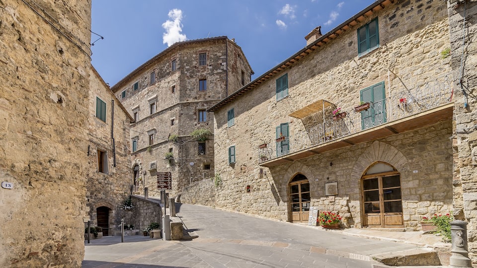 A narrow street with stone buildings, a visible number '13' sign, and a clear blue sky.