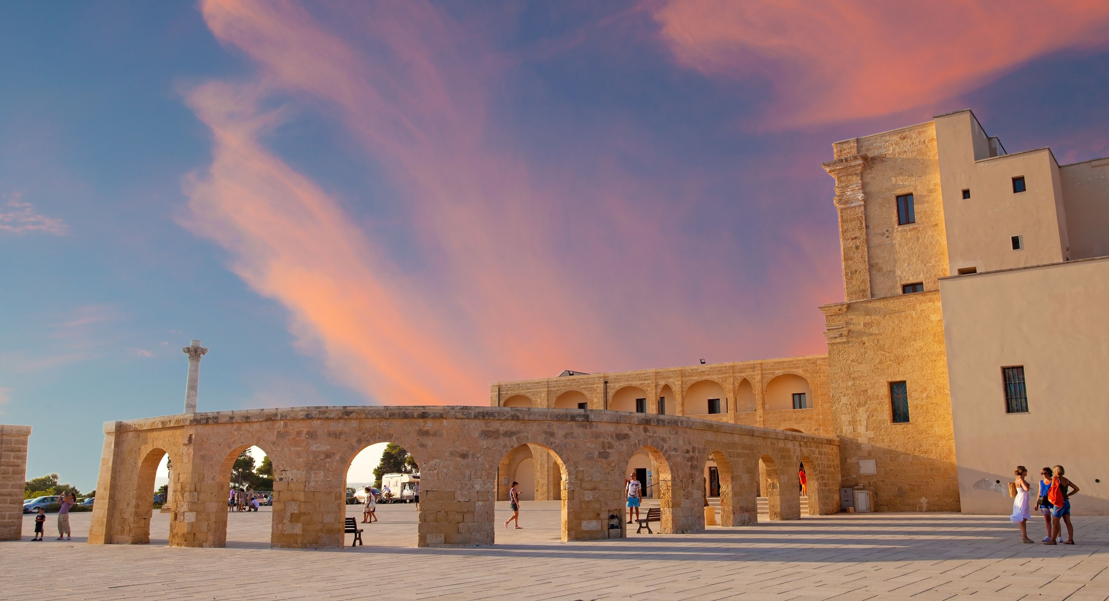 An ancient stone archway with a tower, set against a backdrop of a pink and blue sky.