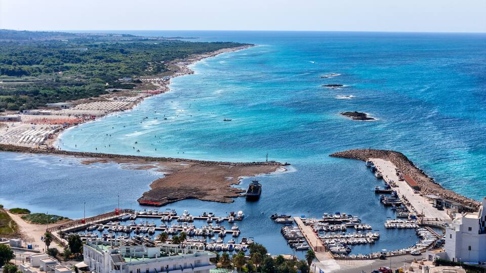 A coastal town with a marina, beach, and rocky outcrops.