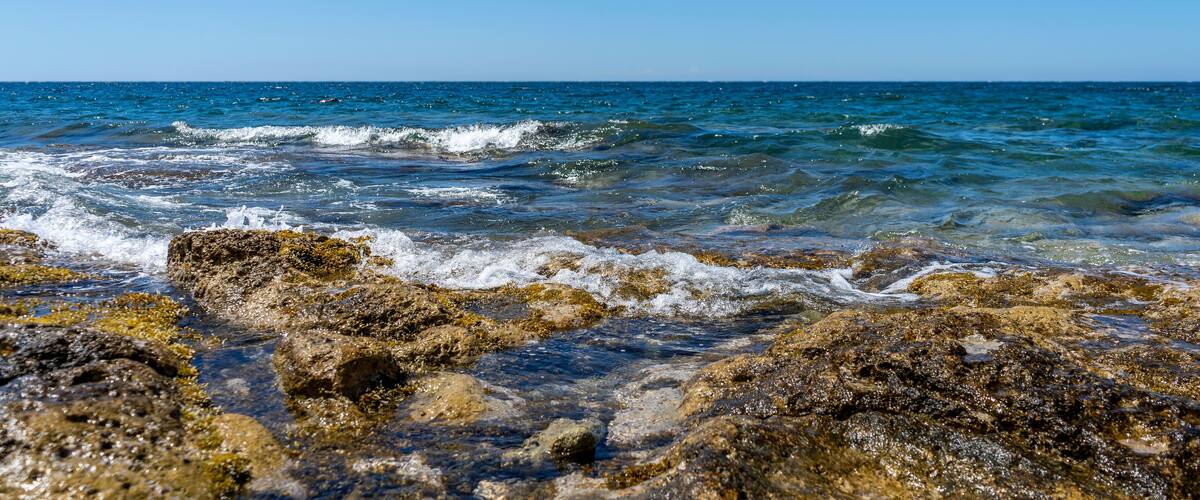 A rocky shoreline with clear blue water and waves crashing against the rocks.