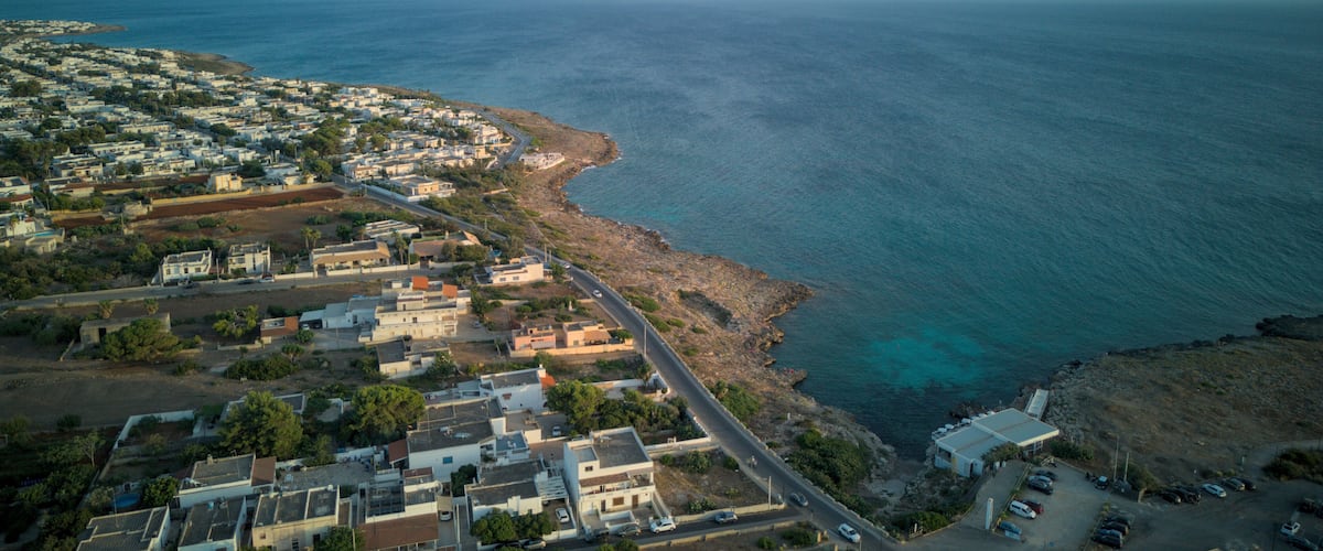 A coastal town with a narrow road along the sea, buildings, and clear blue waters.