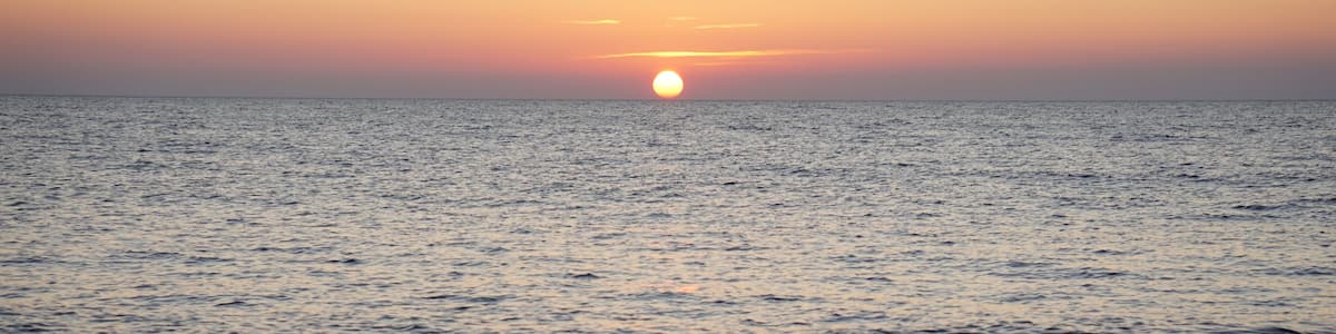 A sunset over a calm sea with rocky coastline in the foreground.