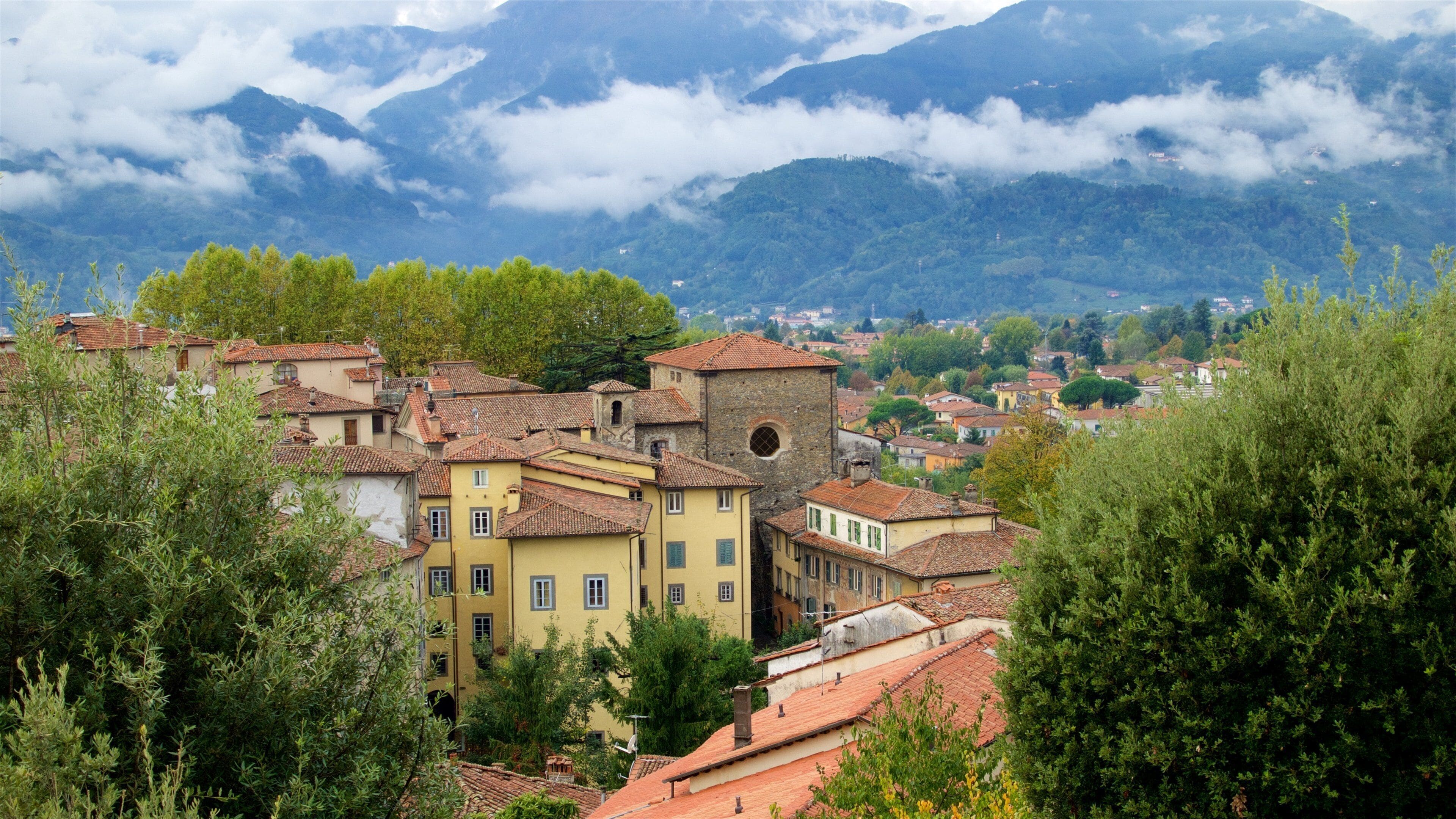 A town with red-tiled roofs, surrounded by lush greenery and mountains in the background.