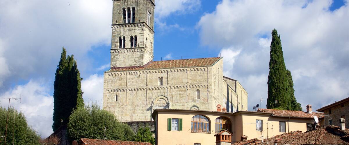 Une église historique en pierre, dotée d’un haut clocher, entourée de bâtiments traditionnels et de grands cyprès.