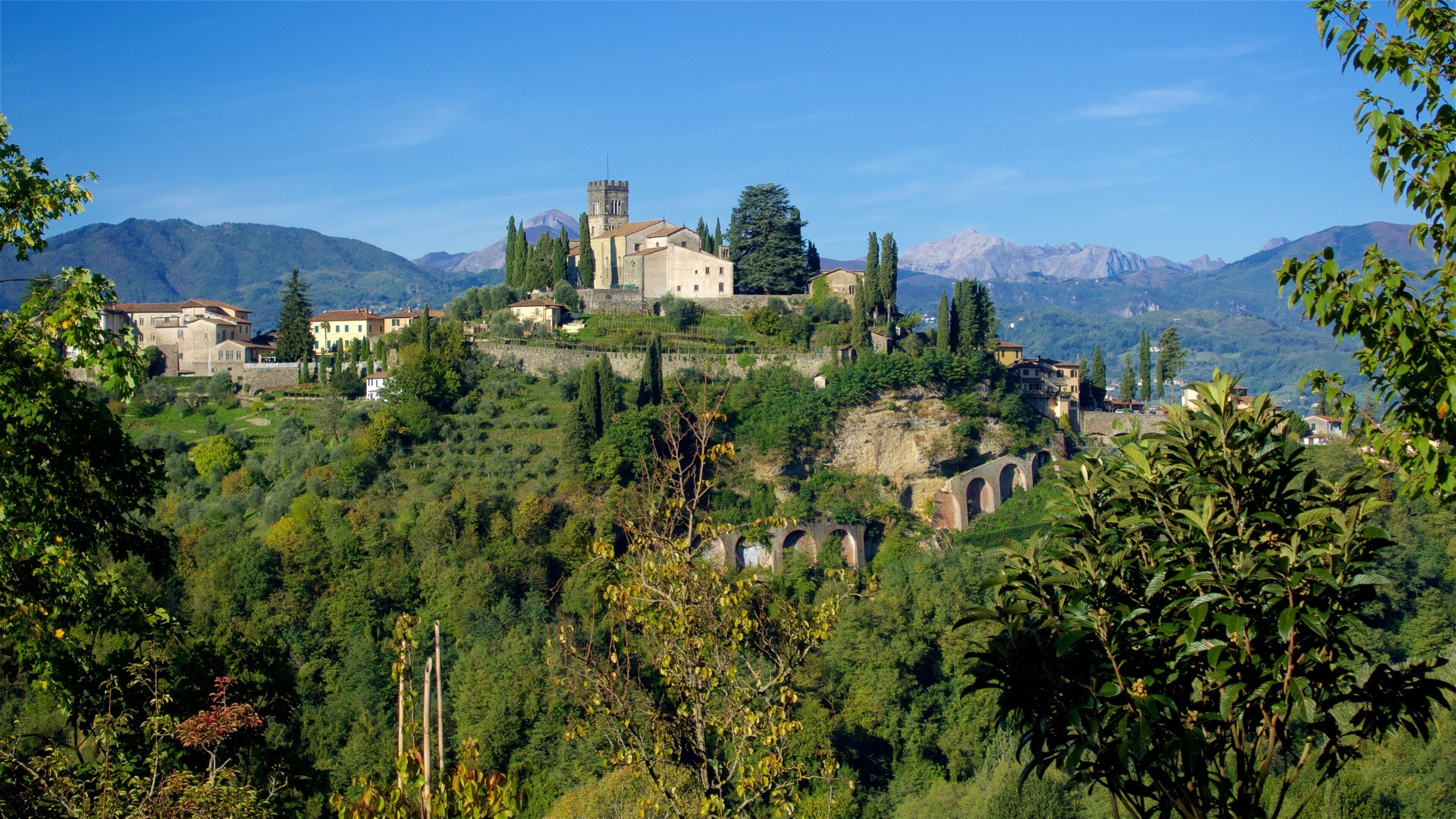 A hillside village with historic stone buildings, a prominent tower, and a lush green landscape.