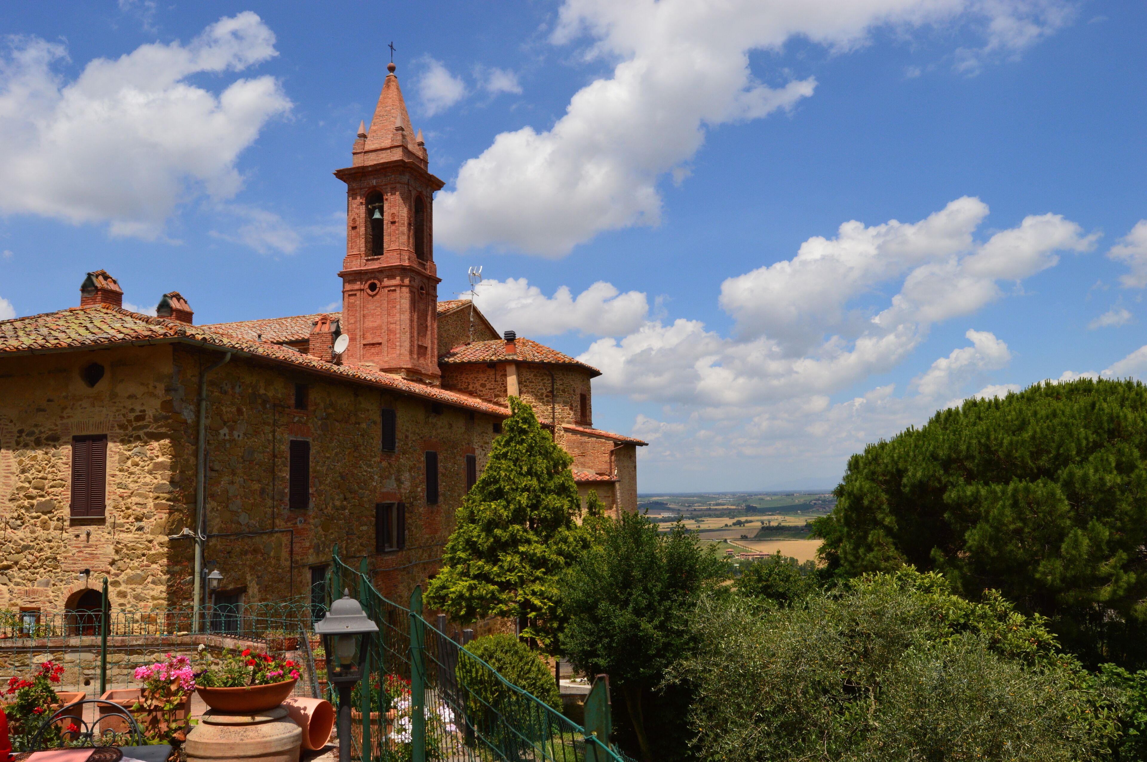A historic stone building with a bell tower, surrounded by lush greenery and a clear blue sky.
