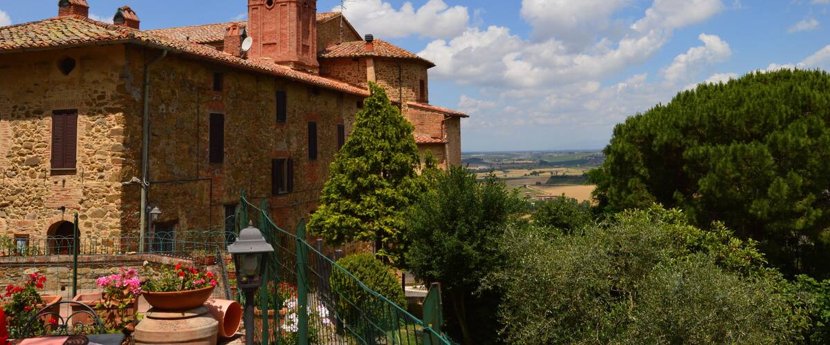 A historic stone building with a bell tower, surrounded by lush greenery and a clear blue sky.