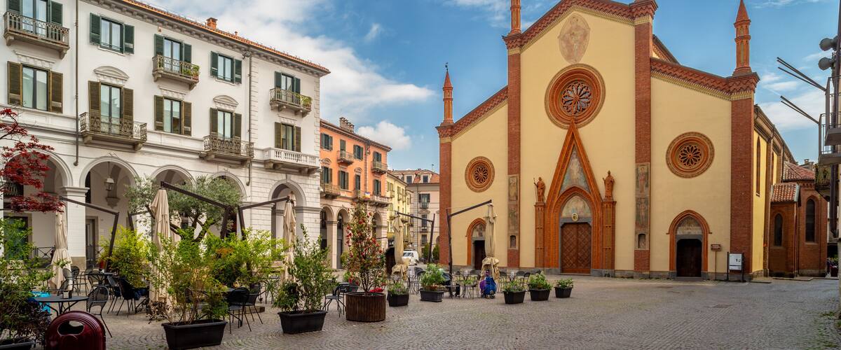 A cobblestone square with historic buildings, a church with a prominent rose window, and potted plants.