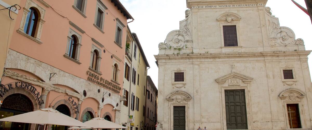 A street with a pink building labeled "Cassa di Risparmio della Provincia di Modena" and a white building with classical architecture.