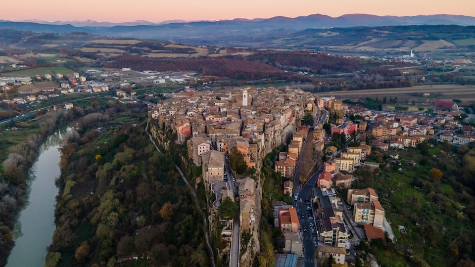An aerial view of a historic town with a river, dense buildings, and surrounding hills.
