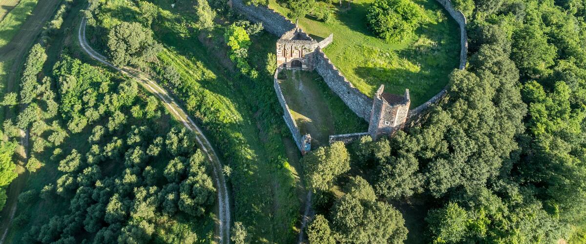 An aerial view of a historic castle surrounded by lush greenery and agricultural fields.