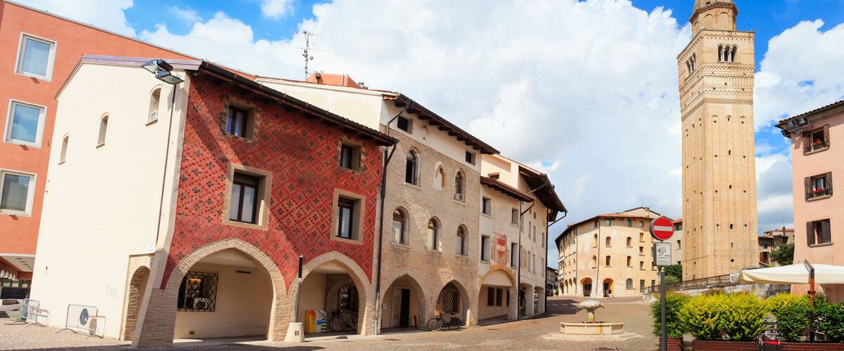 A historic town square with a prominent tower, red and beige buildings, and a fountain.