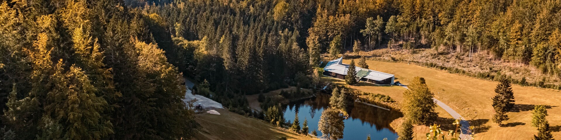 Un paisaje montañoso con un lago, una casa y un bosque.