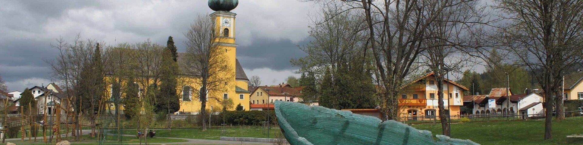 Un bote verde sobre un área cubierta de césped, un estanque y una iglesia con cúpula verde al fondo.